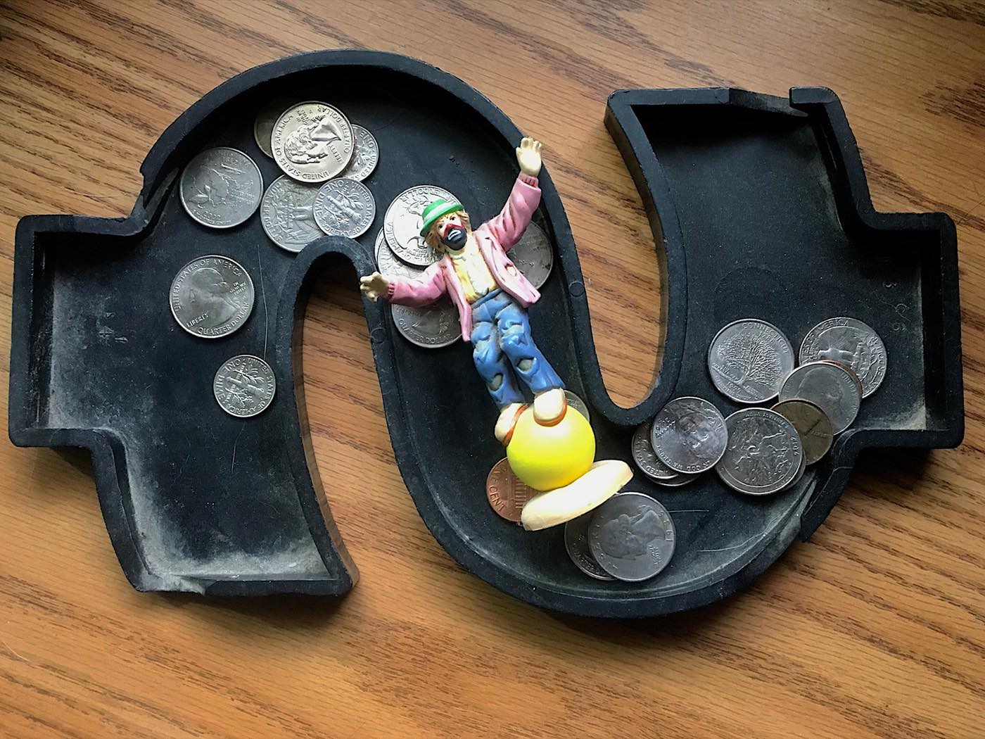 A toy clown balancing on a ball inside a dollar-sign coin tray full of quarters